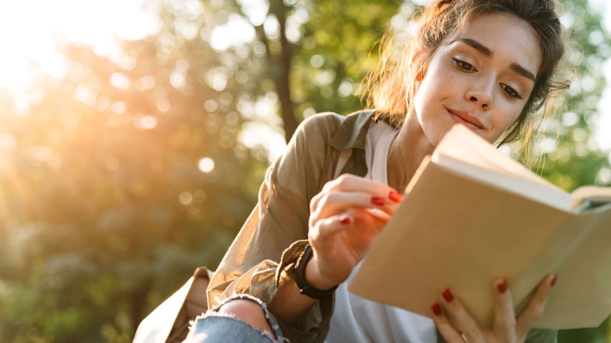 Image of young woman smiling and reading book in green park