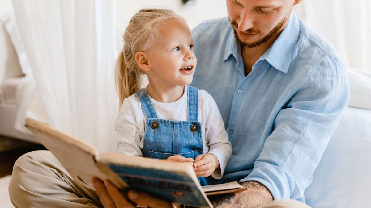 Young white father and little daughter reading book together at home