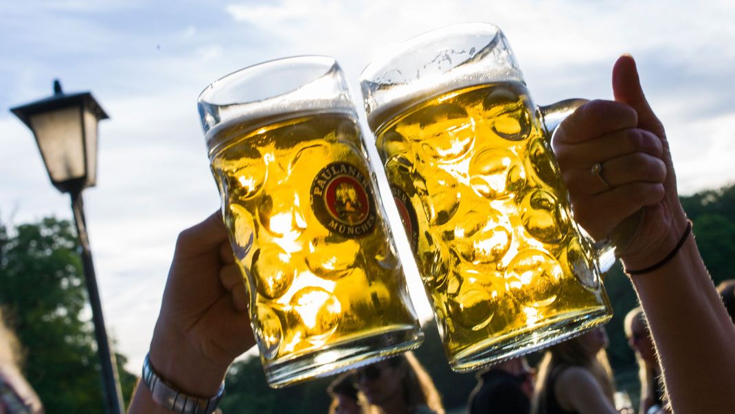 Zwei Personen prosten sich in einem Biergarten mit zwei Maßkrügen zu