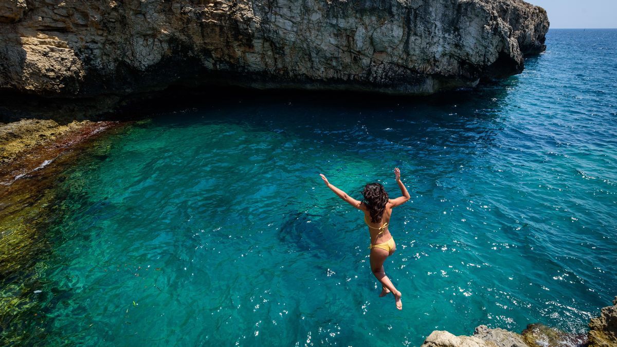 Frau springt von einem Felsen ins Meer