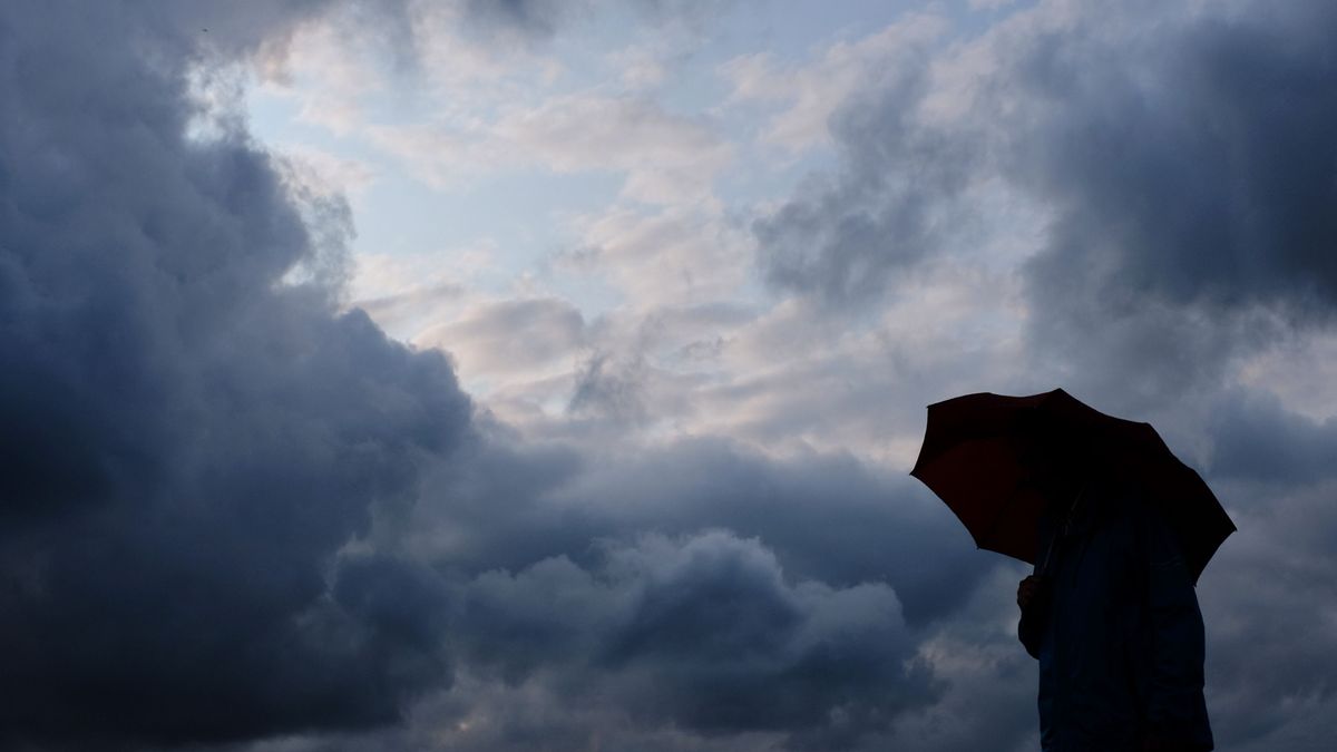 Ein Mann geht mit einem Regenschirm vor aufziehenden dunklen Wolken spazieren.