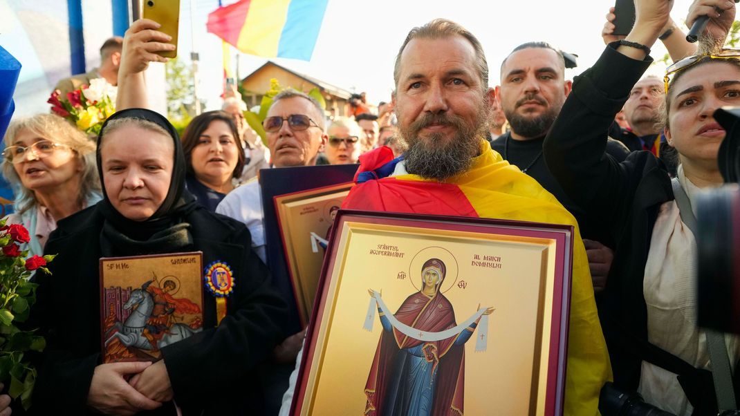 Rumänien, Bukarest: Menschen halten religiöse Ikonen vor dem Wahllokal, in dem Calin Georgescu, der Sieger der ersten Runde der annullierten Wahlen im letzten Jahr, und der Präsidentschaftskandidat George Simion in der ersten Runde der Wiederholung der Präsidentschaftswahlen. 