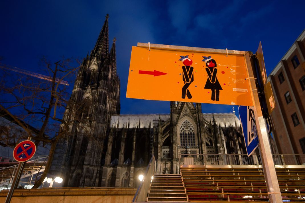 Ein Schild vor dem Dom in Kölle weist den Weg zu den Toiletten für die Feiernden.