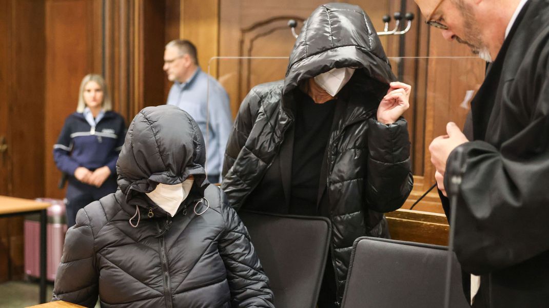 Die beiden angeklagten Lehrerinnen kommen mit Kapuzen auf den Köpfen neben ihrem Anwalt in den Verhandlungssaal in Mönchengladbach.
