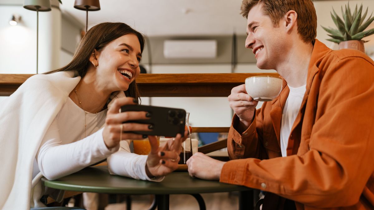 Cheerful couple watching video with smartphone while sitting in cafe