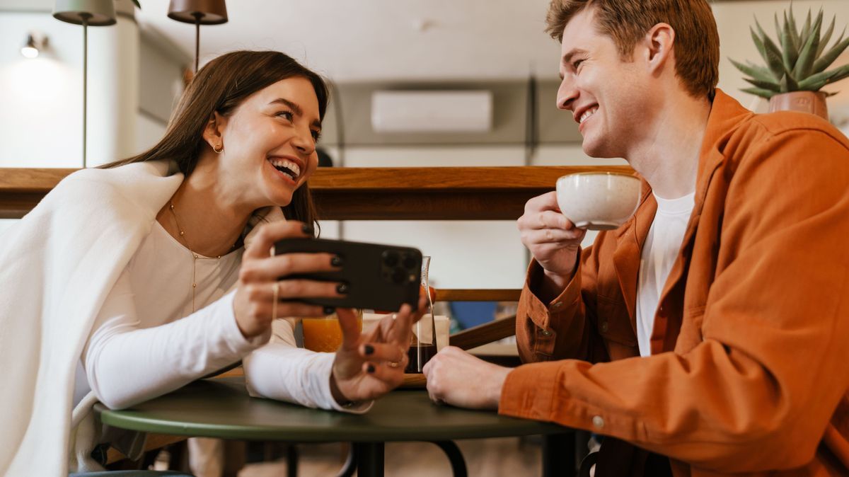 Cheerful couple watching video with smartphone while sitting in cafe