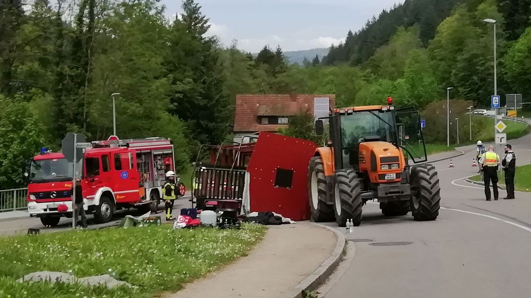 Rettungskräfte stehen nach einem Unfall neben einem einem umgestürzten Maiwagen. 