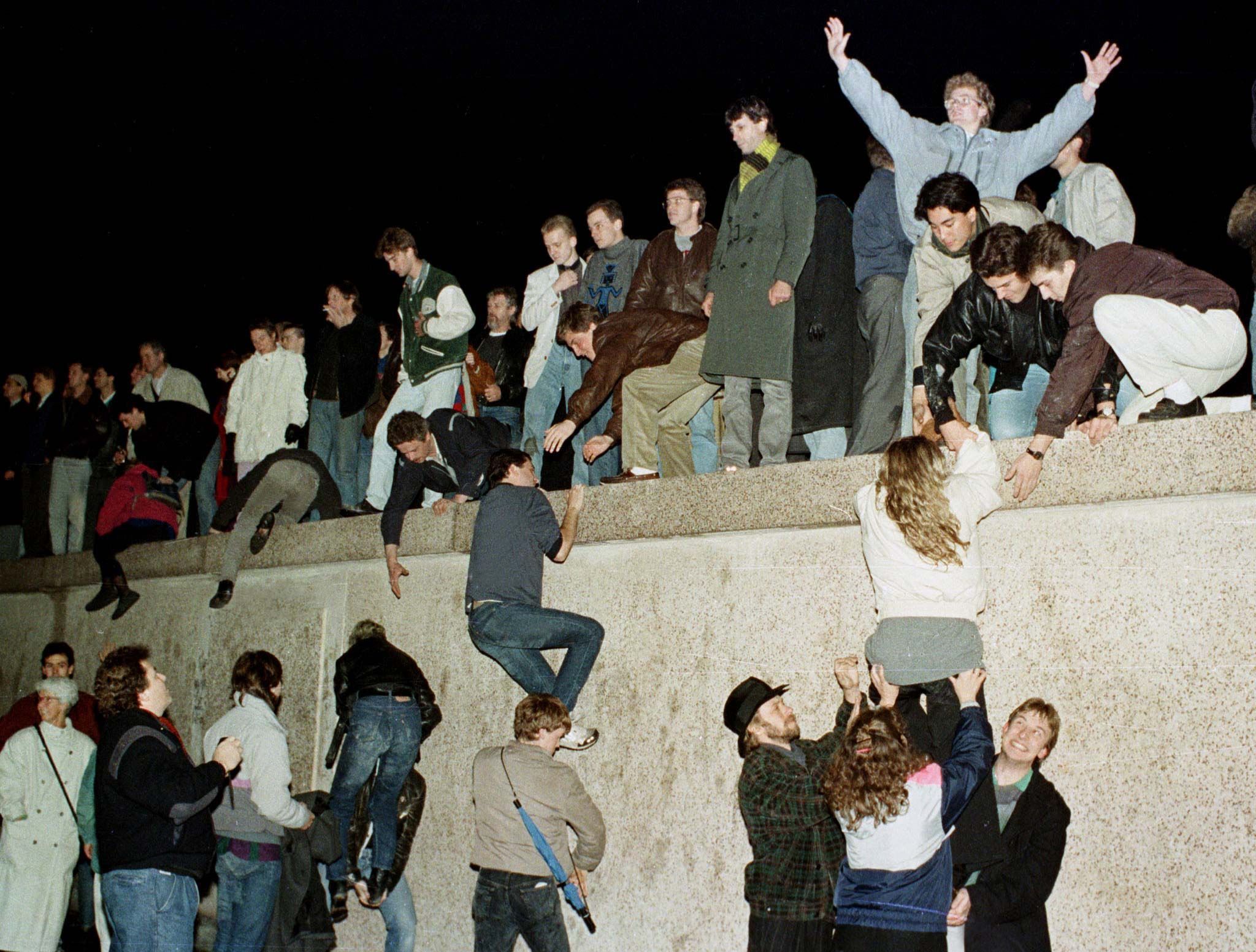 Menschen klettern auf die Berliner Mauer, während sie die Öffnung der DDR-Grenze am 9. November 1989 feiern. 