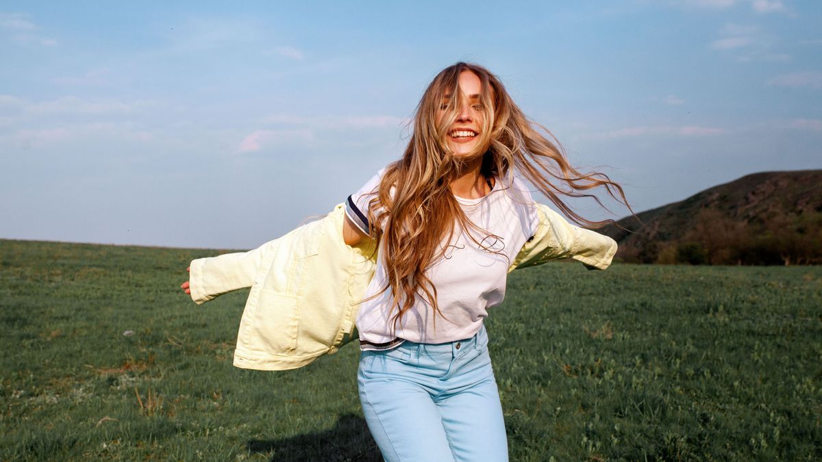 Outdoors lifestyle fashion portrait of happy smilling blonde girl. Beautiful smile. Long curly light hair. Wearing stylish yellow jacket and jeans. Joyful and cheerful woman. Happiness