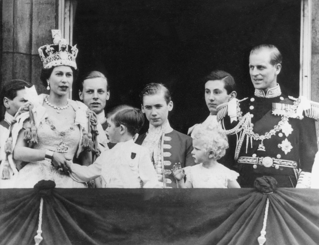 Königin Elizabeth II. kurz nach ihrer Krönung auf dem Balkon des Buckingham Palace. Vorne dreht sich ein Mini-Charles fragend zu seiner Mutter um.