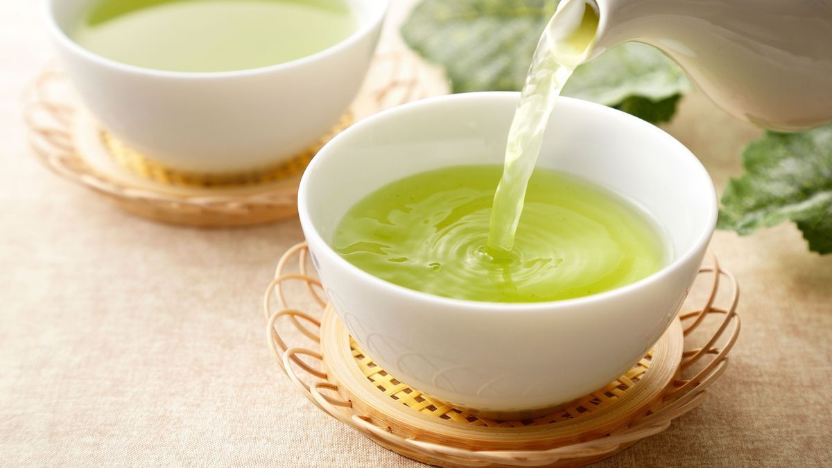 Kanne, aus der grüner Tee in eine Tasse geschenkt wird.