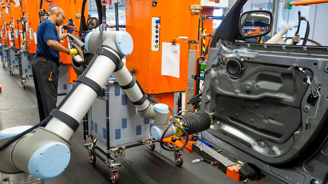 Ein Roboter und ein Arbeiter arbeiten in der Produktion im BMW-Werk an einem neuen Auto.