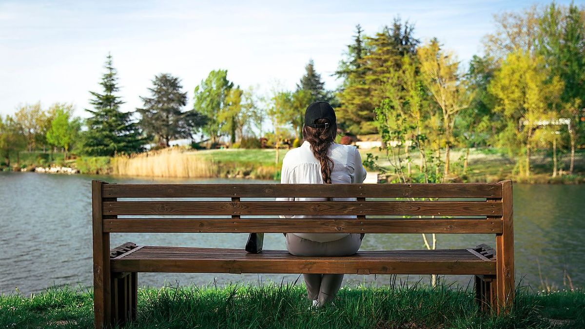 Young woman sitting on bench in front of lake at park