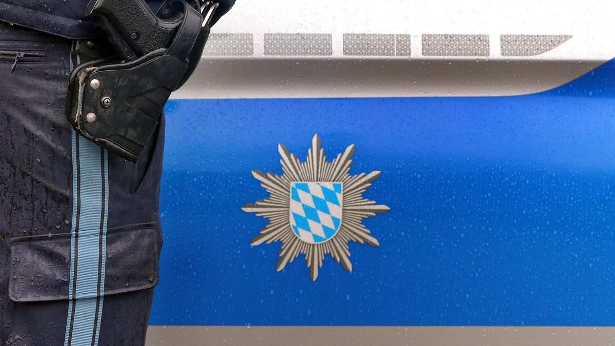 Ein Polizist mit Handschellen und einer Pistole am Gürtel steht vor einem Streifenwagen.