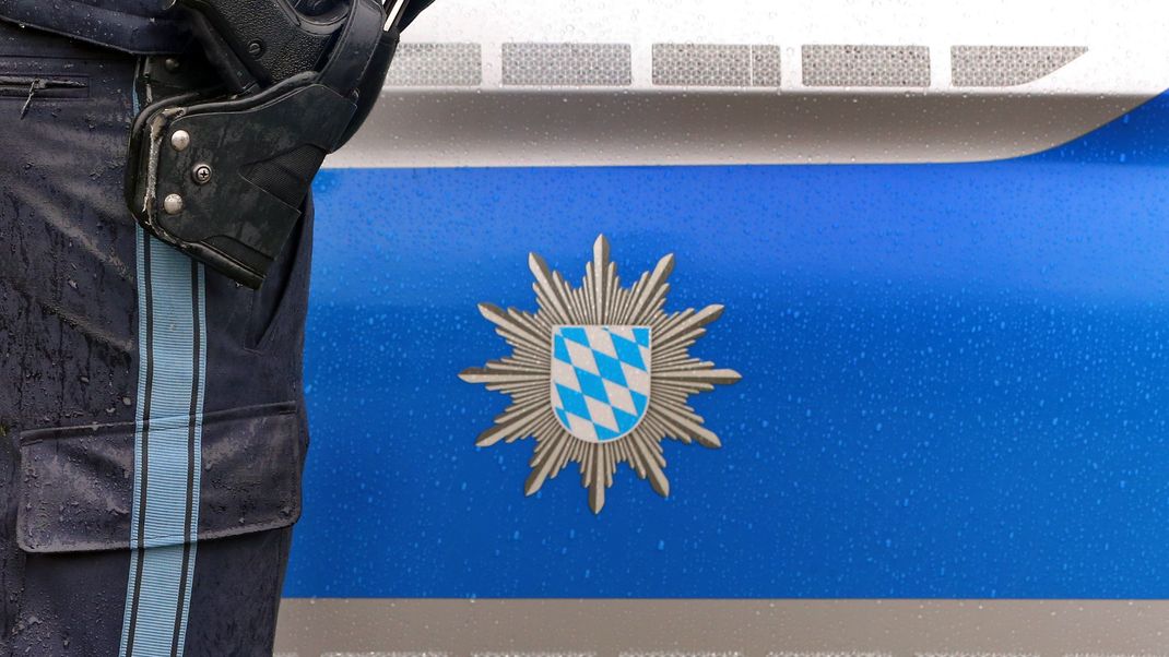 Ein Polizist mit Handschellen und einer Pistole am Gürtel steht vor einem Streifenwagen.