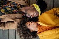 Top view of trendy African American man and woman in bright coat lying opposite with face to face looking at each other