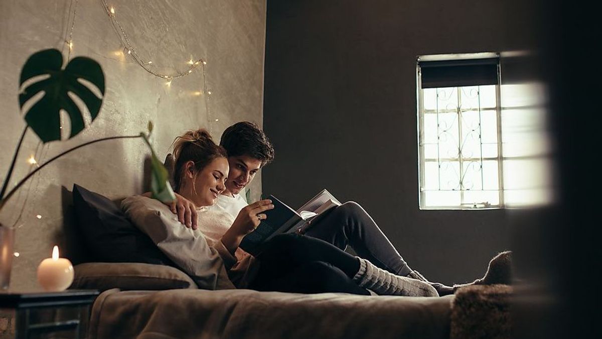 Young man and woman resting on bed with a book. Couple relaxing on bed and reading book.