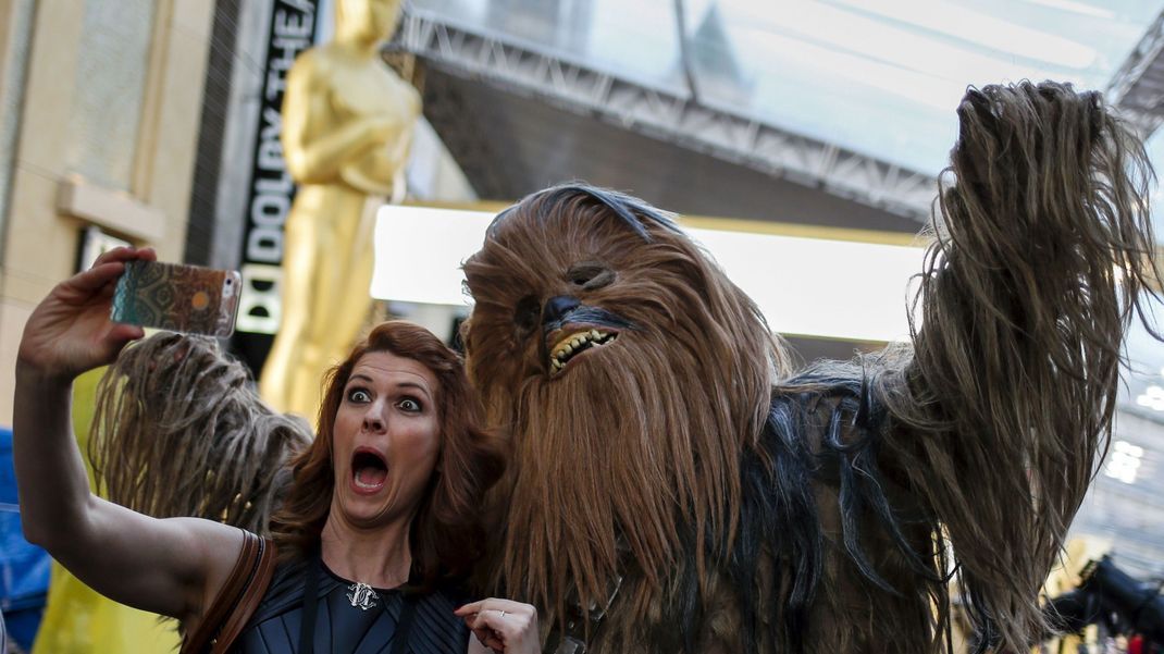 Eine Frau posiert mit einer Chewbacca-Figur vor einer großen Oscar-Statue.