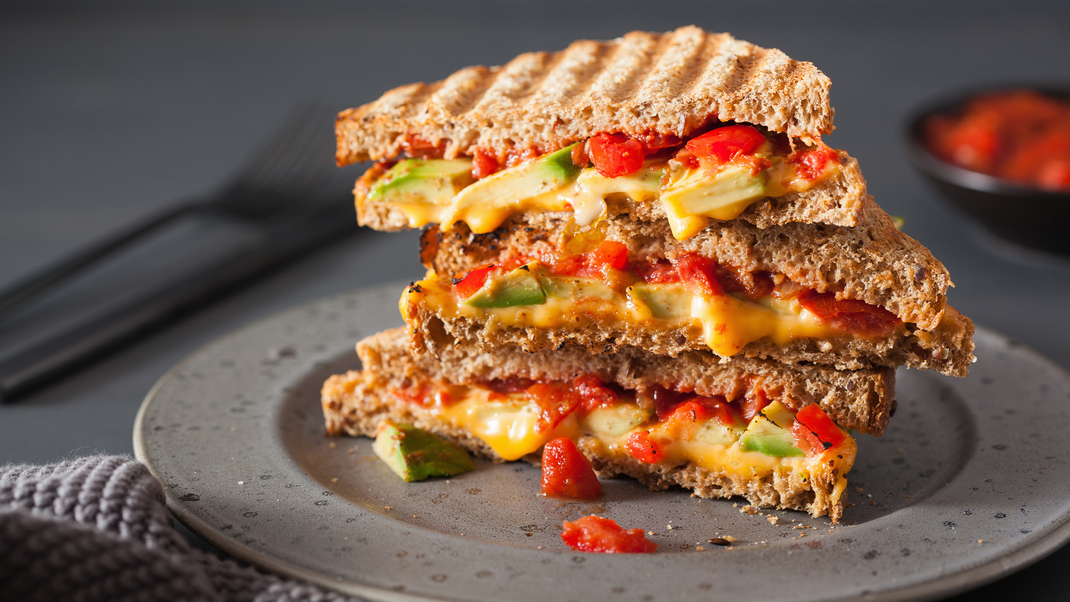 Genussvolle Versuchung: Gegrilltes Avocado-Sandwich mit geschmolzenem Käse, Bacon und Tomaten.