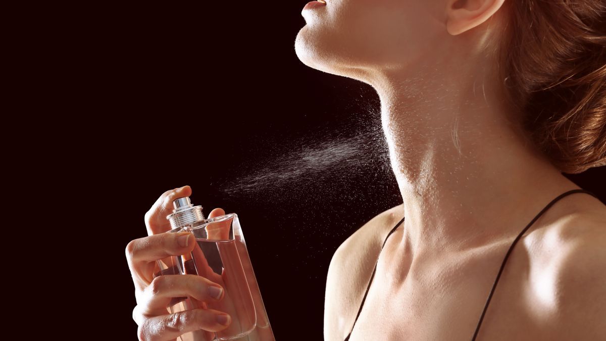 Beautiful young woman with bottle of perfume on dark background