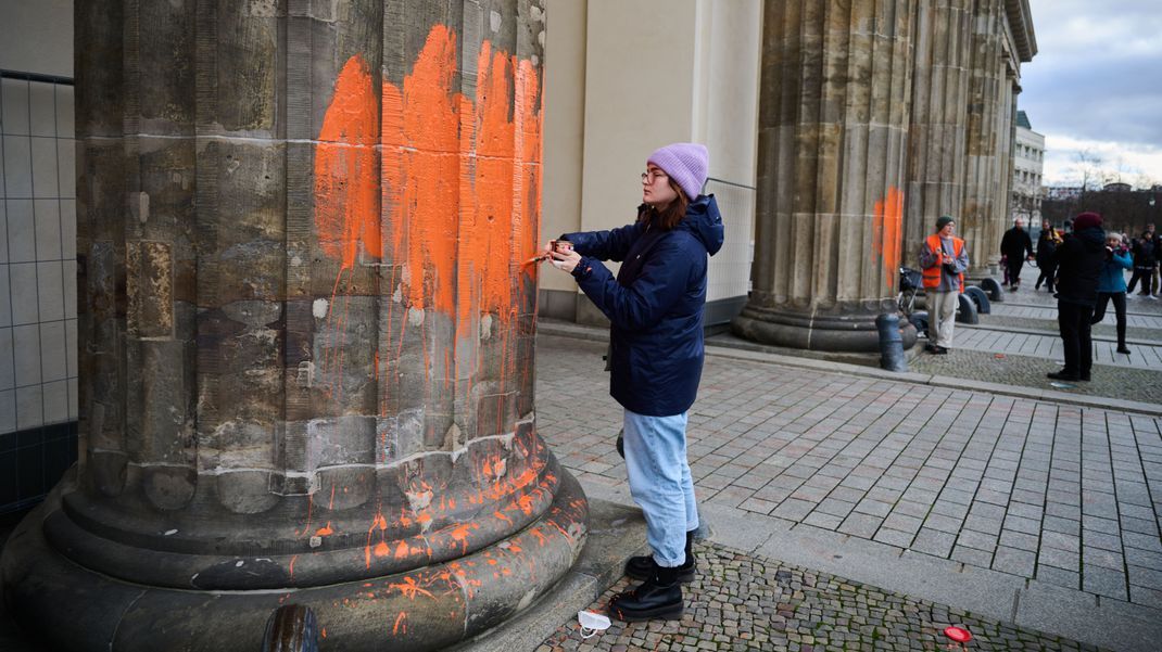 Zwei Klimaaktivistinnen bemalen das Brandenburger Tor mit oranger Farbe. 