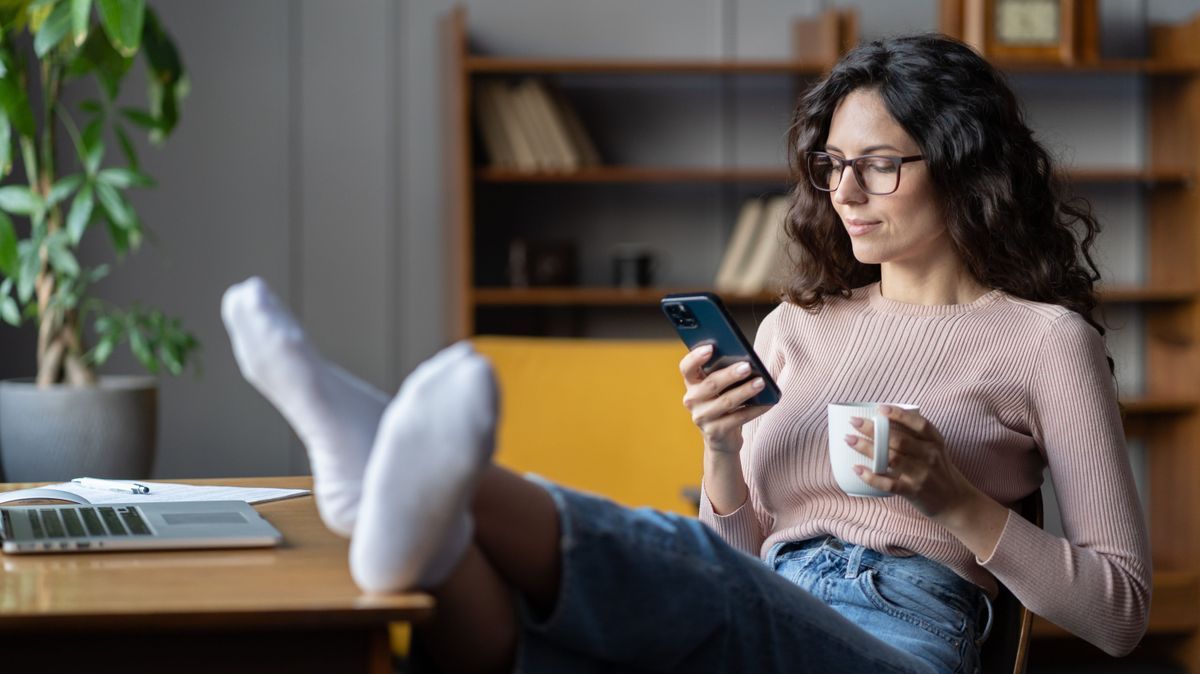 Woman freelancer procrastinate from work. Female distracted from laptop scroll social media on phone