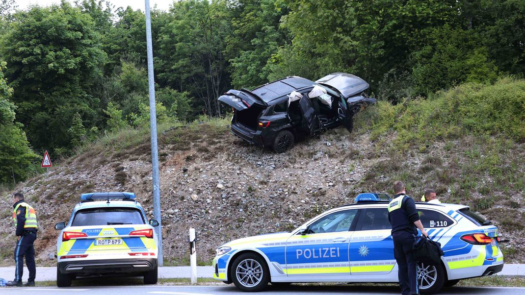 Zwei Polizeiwagen stehen vor einem verunfallten Auto, das auf einer Böschung steht.