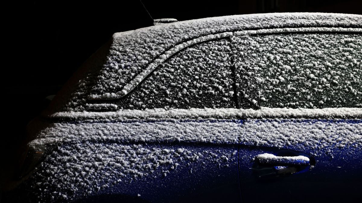 Ein mit einer leichten Schneedecke überzogenes Auto steht am Abend auf einem Parkplatz.