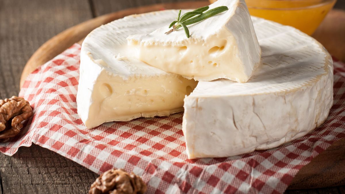 Brie type of cheese. Camembert cheese. Fresh Brie cheese and a slice on a wooden board with nuts, honey and leaves. Italian, French cheese.