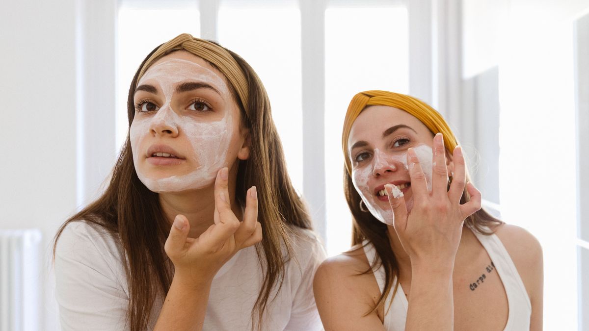 Two girl friends apply clay mask on face at home