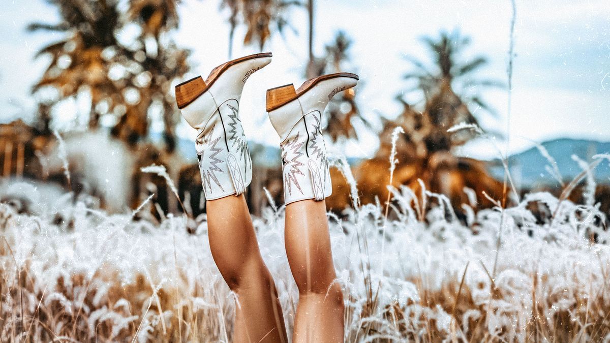 close up of young woman legs wearing cowgirl boots on the field at sunset