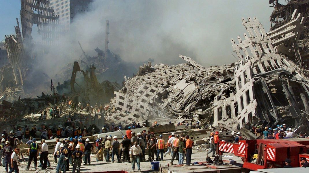 13.09.2001, USA, New York: Rettungskräfte setzen ihre Suche nach Opfern fort, während Rauch aus den Trümmern des World Trade Center aufsteigt. 