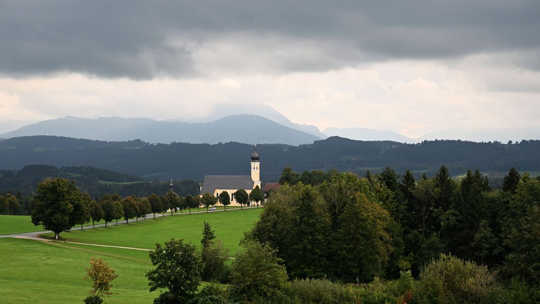 Dunkle Wolken sind über den Bergen hinter der Wallfahrtskirche Wilparting am Irschenberg zu sehen. 
