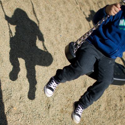 Der Schatten eines Mannes und eines schaukelnden Kindes fallen auf einem Spielplatz.