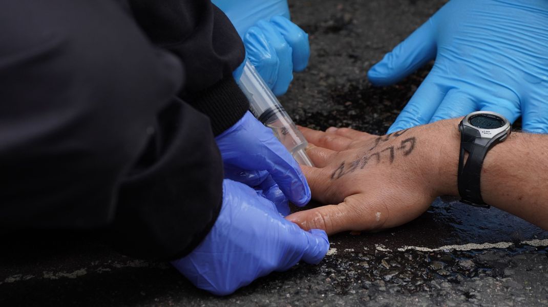 Polizisten versuchen die Hand eines Klimaaktivisten, der sich auf die Fahrbahn der London Bridge geklebt hat, zu befreien.