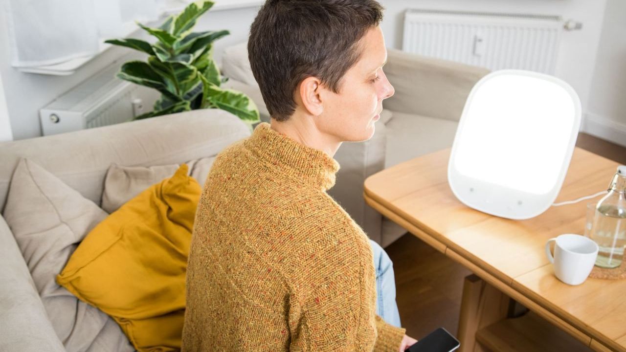 Lichttherapie - eine Frau sitzt vor einer Tageslichtlampe