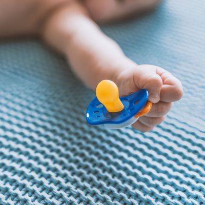 Baby with a nipple. Close up of baby hands with pacifier. Focus is on hands. Newborn sleeping on a blanket holding a pacifier in his hand. Baby is lying happy holding baby nipple soother in hand