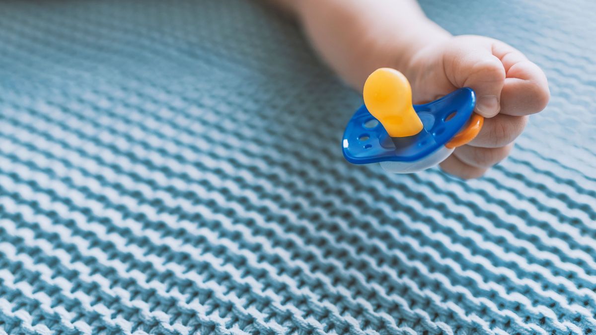 Baby with a nipple. Close up of baby hands with pacifier. Focus is on hands. Newborn sleeping on a blanket holding a pacifier in his hand. Baby is lying happy holding baby nipple soother in hand