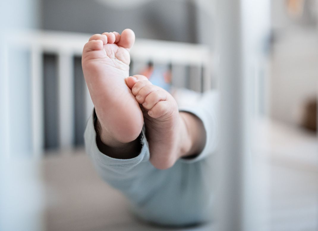 Die Füße eines Babys sind in einem Kinderbett zu sehen.