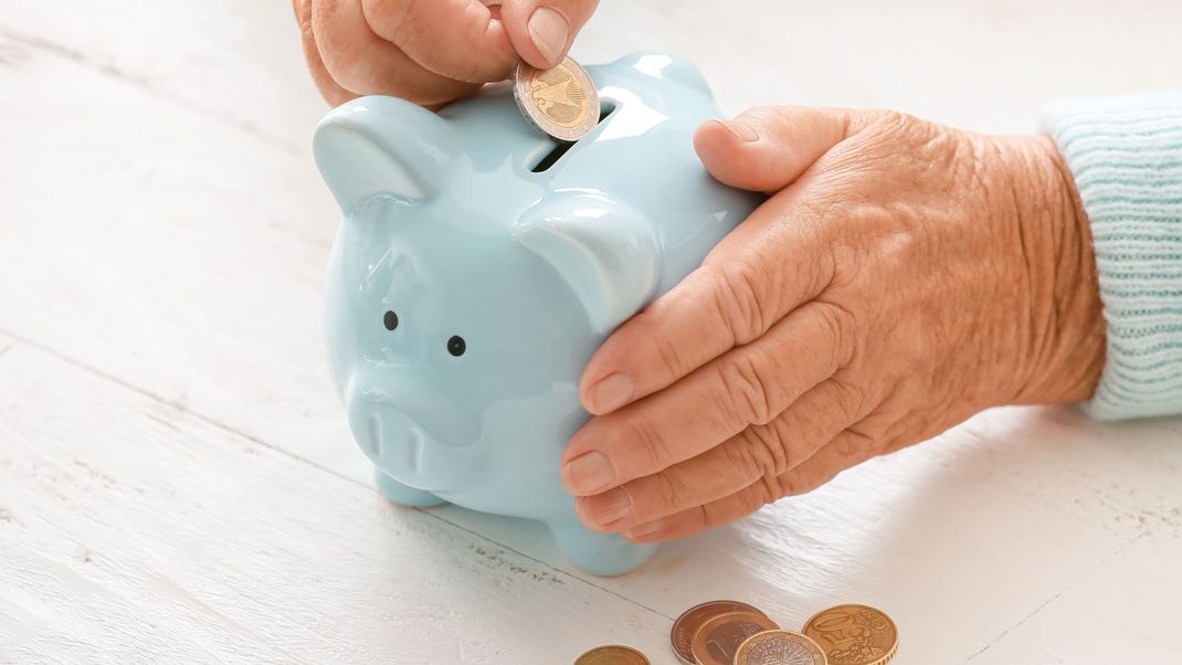 Senior woman putting coin into piggy bank at table. Concept of pension