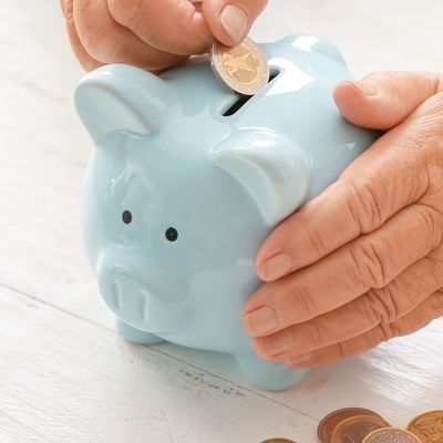 Senior woman putting coin into piggy bank at table. Concept of pension