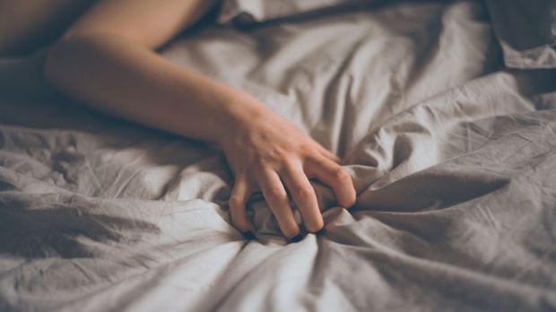 Eine Hand krallt sich in ein Bettlaken. 