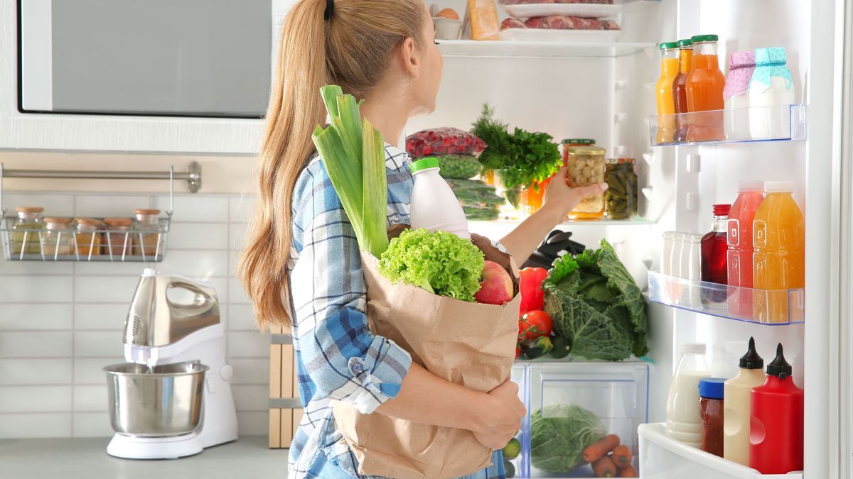Woman putting products into refrigerator in kitchen