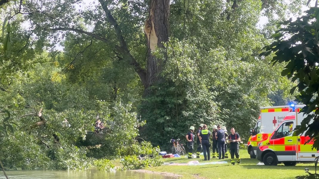 4. August 2024, München: Rettungskräfte stehen an der Unglücksstelle im Englischen Garten in München, an der ein großer Ast abbrach, auf zwei Menschen fiel und diese verletzte. 