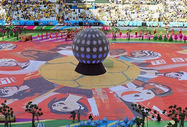 
                <strong>Natur, Menschen, Fußball</strong><br>
                Zu Beginn dreht sich in der Mitte der Arena eine riesige LED-Weltkugel, dazu haben sich Tänzer und Tänzerinnen grün gekleidet, um den Urwald und Dschungel Brasiliens widerzuspiegeln.
              