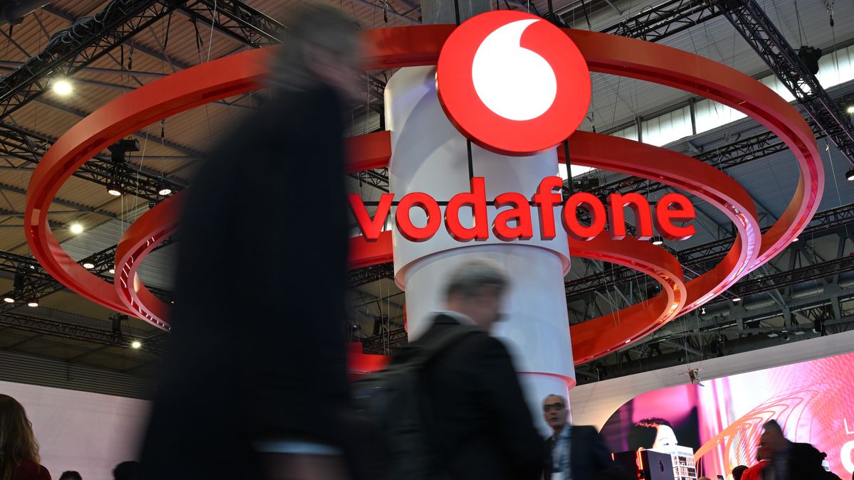 3. März 2025, Spanien, Barcelona: Menschen gehen auf der Mobilfunk-Messe Mobile World Congress (MWC) am Stand des Telekommunikationskonzerns Vodafone vorbe