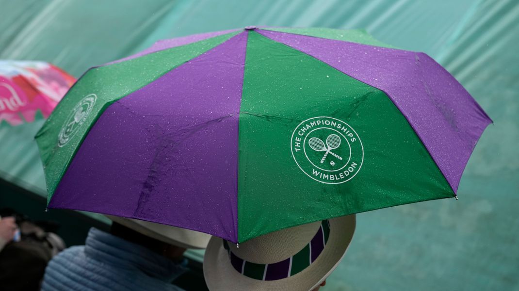 Wimbledon: Menschen schützen sich mit Regenschirmen, nachdem ein Spiel wegen des Regens unterbrochen werden musste. 