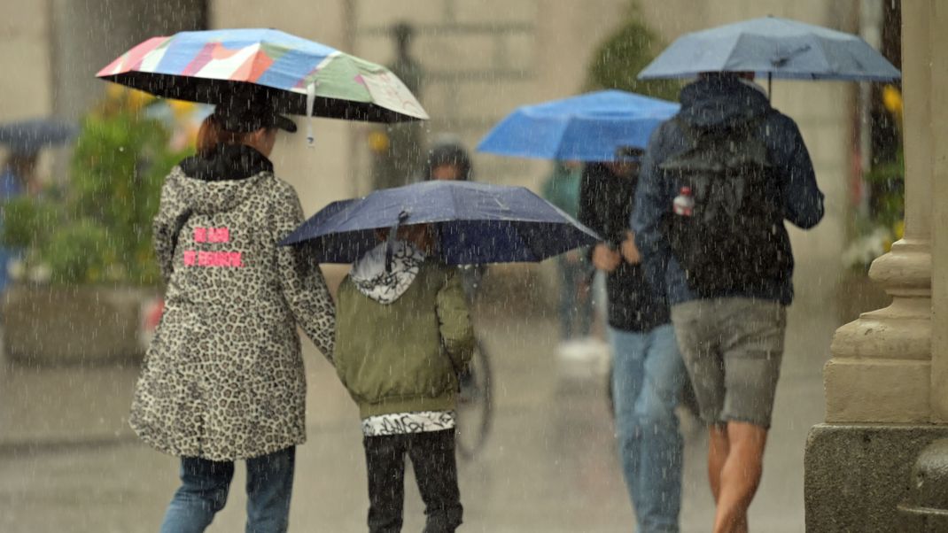 Passanten gehen mit Regenschirmen durch die Altstadt.