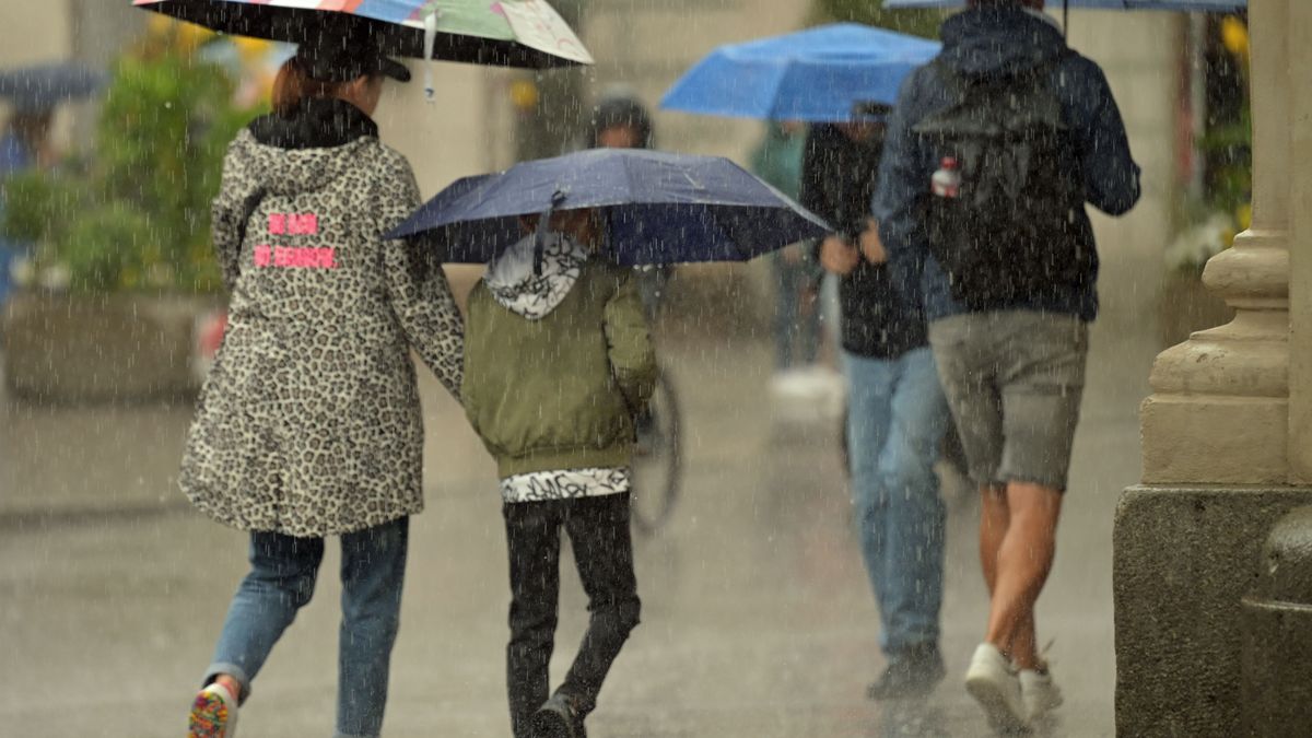 Passanten gehen mit Regenschirmen durch die Altstadt.