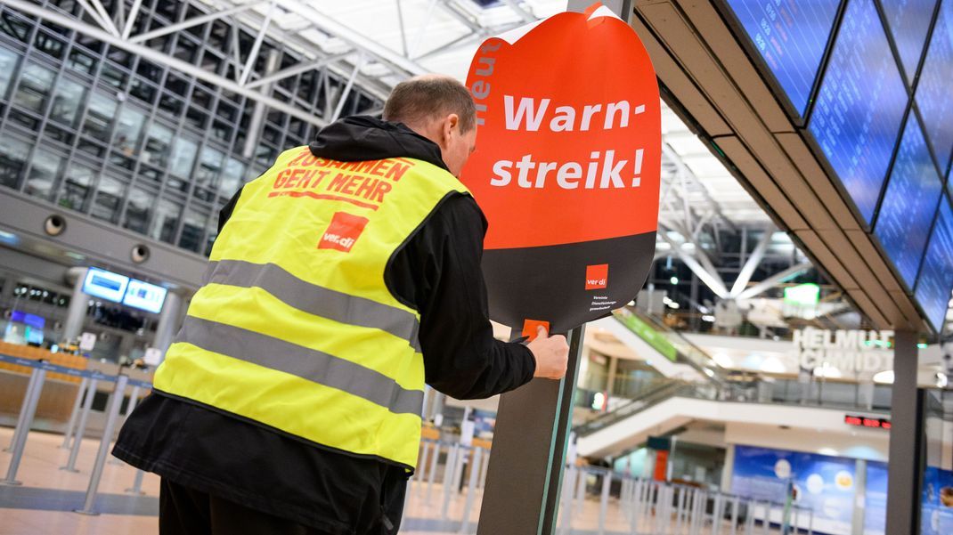 Archivbild: Ein Gewerkschaftsvertreter klebt ein Plakat mit der Aufschrift "Warnstreik!" und einen Flyer an die Anzeigetafel im leeren Terminal 2. 